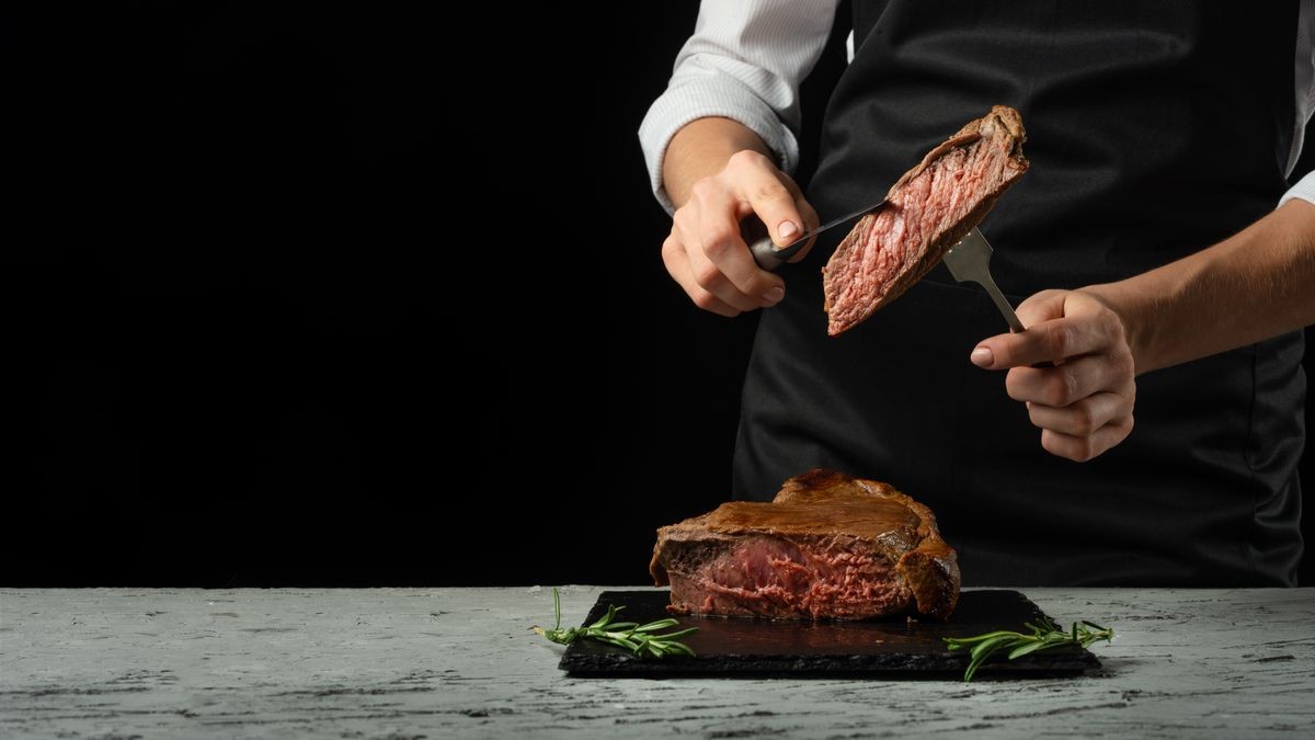 Chef, cut with a meat steak on a black background with an open space for text or restaurant menus. Horizontal photo Black text area.